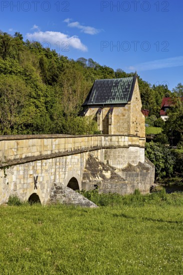 An old stone bridge with a small chapel in the background, surrounded by green trees under a blue sky, The historic Werra Bridge at Creuzburg in Thuringia