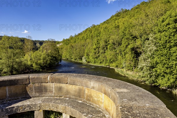 Stone bridge with a view of a river and green hills in the background, view from the historic Werra bridge over the Werra to the Ebenauköpfen near Creuzburg in Thuringia