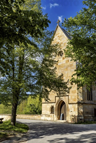 A Gothic church made of sandstone surrounded by trees under a bright blue sky, the Liborius Chapel on the Werra Bridge near Creuzburg in Thuringia
