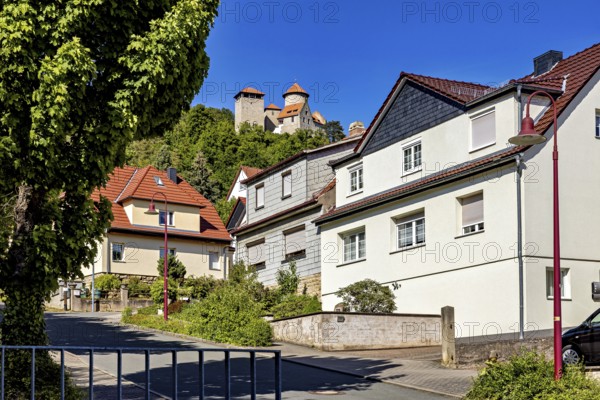 Rural houses on the roadside with a historic castle on the hill in the background, Normannstein Castle near Treffurt in Thuringia