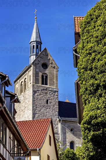 Church with high tower in front of blue sky and surrounding buildings, surrounded by trees, The church of the town Treffurt in Thuringia