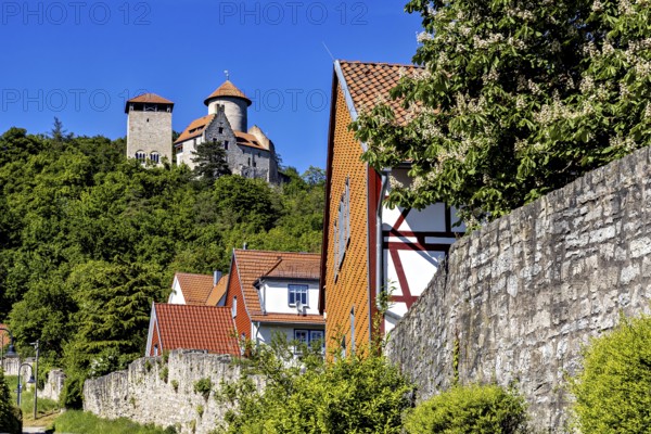 Half-timbered houses in a village in front of an imposing towering castle on a green hill, Normannstein Castle near Treffurt in Thuringia