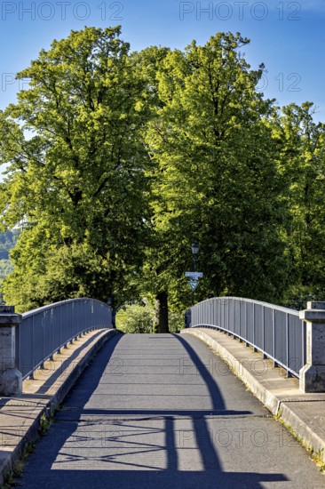 A quiet bridge with railings leads through green trees under a sunny blue sky, The Lauchröder Bridge to Lindenallee near Herleshausen and Lauchröden between Hesse and Thuringia