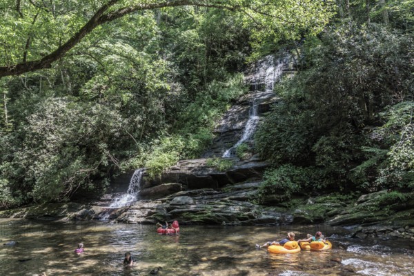 Visitors swimming and floating on inflatables at the base of Tom Branch Falls along Deep Creek in the Smoky Mountains near Bryson City, North Carolina, USA