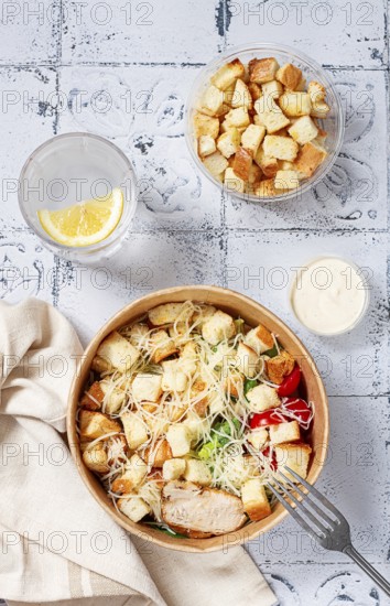 Caesar salad in a paper container, take it on the way, with sauce and croutons, on the table, snack, natural light, no people