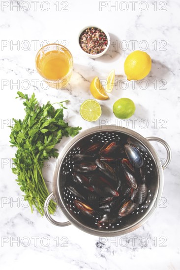 Fresh mussels, in a metal colander, with ingredients on the table, light background, no people