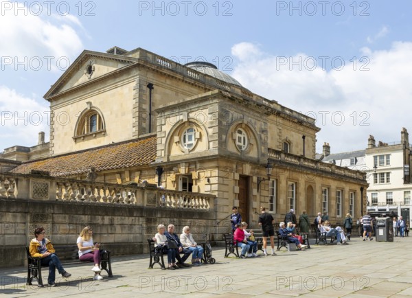 People relaxing next to Roman Baths building, Abbey church yard, city of Bath, north east Somerset, England, UK
