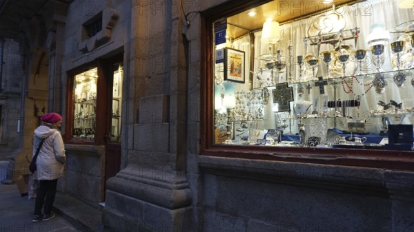 A woman looks at the window of a shop for church devotional items in Santiago de Compostela, making pilgrimages on the Caminho Portugues, Spain