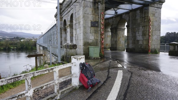 Old stone bridge, with arched construction, a hiking backpack leaning against a railing during a break, pilgrimage on the Caminho Portugues, Portugal