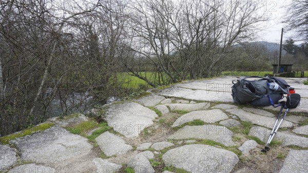 A hiking backpack and hiking sticks on stone slabs of a bridge, making a pilgrimage on the Caminho Portugues, Portugal