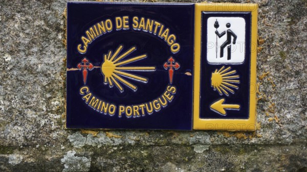 Guide on the Camino de Santiago with yellow arrow symbolism and cross, scallop on a stone wall, pilgrimage on the Caminho Portugues, Portugal