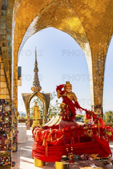 Round arch pavilions decorated with colorful mosaics and glass works of art, including a gilded statue on a red base, Buddhist temple complex Wat Phra That Sorn Kaew, Phetchabun province, Thailand