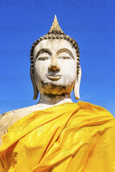 Stone Buddha statue decorated with yellow cloths, historic Buddhist temple complex, Ayutthaya, Thailand