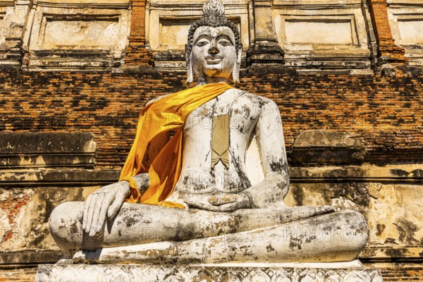 Stone Buddha statue decorated with yellow cloth, historic Buddhist temple complex, Ayutthaya, Thailand