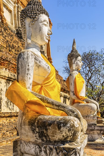 Stone Buddha statues decorated with yellow cloths, historic Buddhist temple complex, Ayutthaya, Thailand
