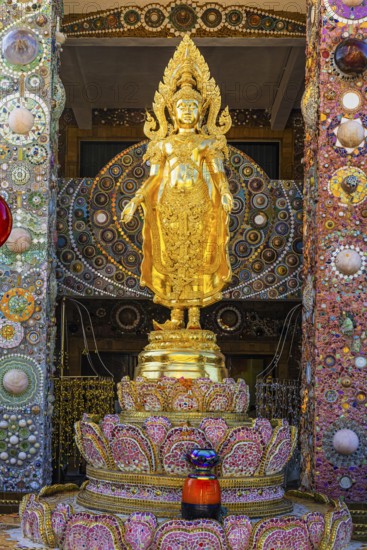 Gilded standing Buddha statue on a base decorated with mosaics and glass works of art, Buddhist temple complex Wat Phra That Sorn Kaew, Phetchabun province, Thailand