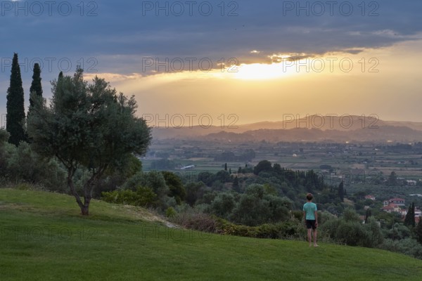 Person standing in the foreground, looking at a vast landscape in the evening light, Hotel Europa, garden restaurant and view of the surrounding landscape, Olympia, Peloponnese, Greece