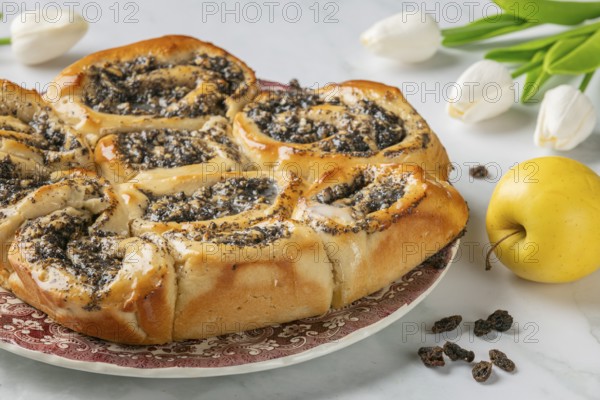 Freshly baked poppy seeds on a plate, next to tulips and an apple