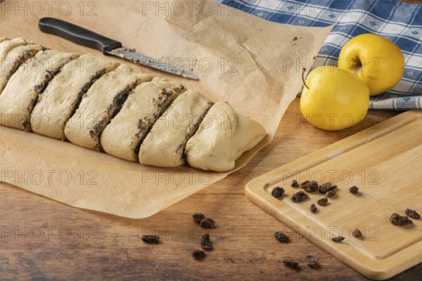 Dough pieces with poppy seed filling on baking paper, next to apples and raisins