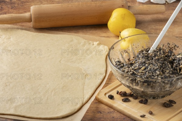 Rolled dough with poppy and raisin mixture in glass bowl, apple next to it