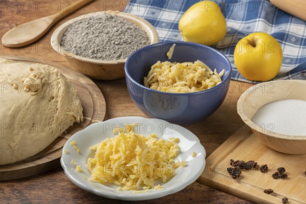Grated apples in a bowl, dough, poppy seeds and sugar for baking preparation on the table
