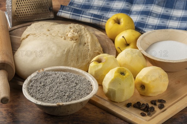 Dough with peeled apples, poppy seeds, sugar and raisins on a wooden table