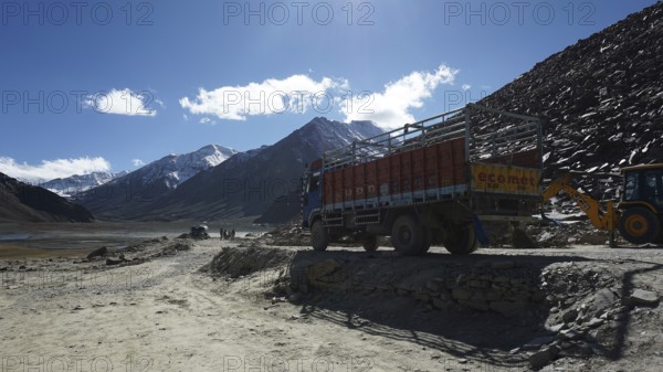 A truck parks on a mountain road with construction sites and mountains in the background, trekking in Ladakh, Himalayas, India