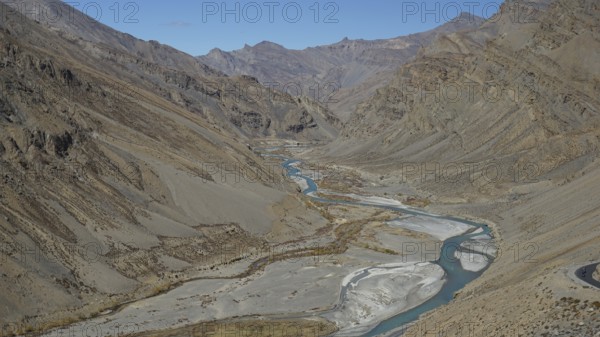 Shimmering blue Indus meanders through a barren valley under a blue sky, trekking in Ladakh, Himalayas, India