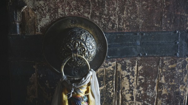 Detail of an old wooden door of a Buddhist monastery with metal ring and rope, surrounded by a dark, textured surface, trekking in Ladakh, Himalayas, India