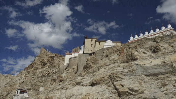 Buddhist monastery on a rocky slope under a bright blue sky with white clouds, trekking in Ladakh, Himalayas, India