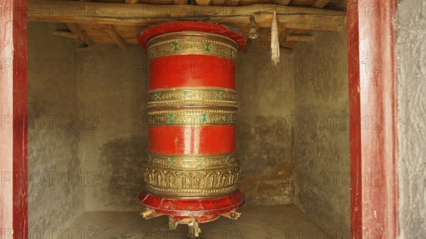 A large red prayer wheel decorated with decoration in a temple-like room, trekking in Ladakh, Himalayas, India