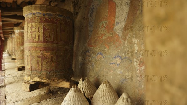 A series of ancient prayer wheels in front of a painted wall in a Buddhist temple, trekking in Ladakh, Himalayas, India
