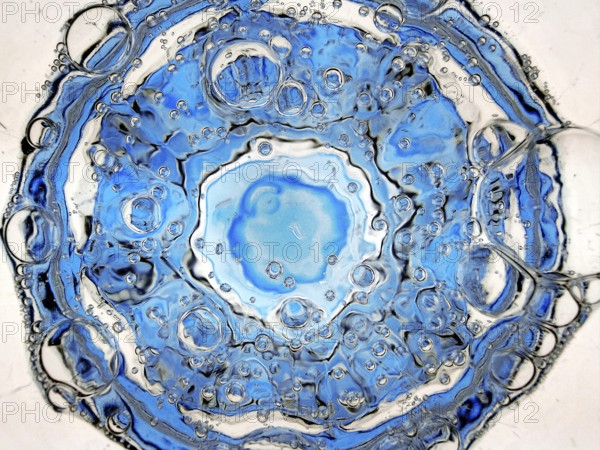 Rising carbon dioxide bubbles in a full water glass with a blue bottom seen from above, detail, Witten, North Rhine-Westphalia, Germany