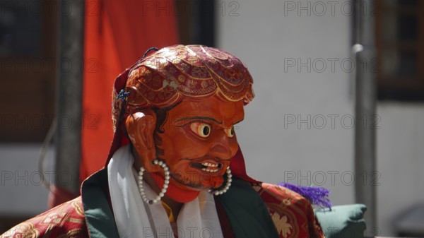 A vivid red-orange masked figure at a Buddhist ritual or dance in Leh, trekking in Ladakh, Himalayas, India