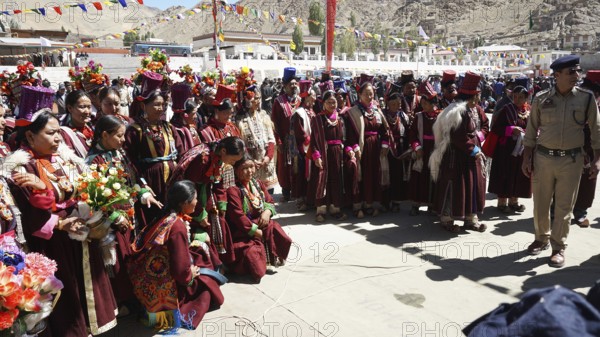 A large group in traditional costume gathers during a cultural festival in Leh, some carrying flowers, trekking in Ladakh, Himalayas, India