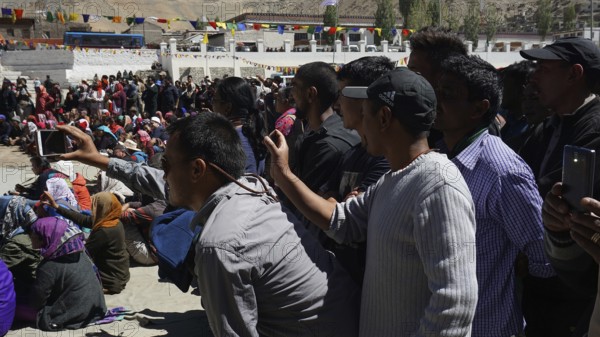 A crowd films an outdoor festival with smartphones, colorful details in the background, Leh, trekking in Ladakh, Himalayas, India