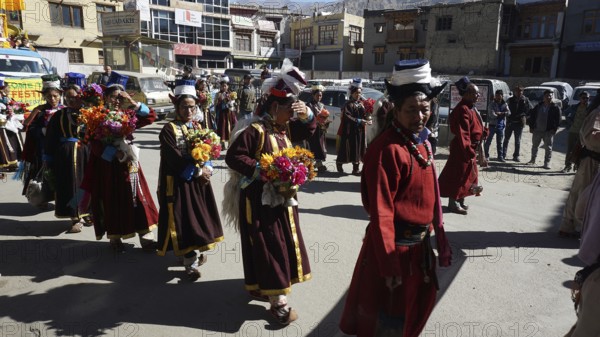 People wearing traditional garments carry flowers during a festive procession in Leh, trekking in Ladakh, Himalayas, India