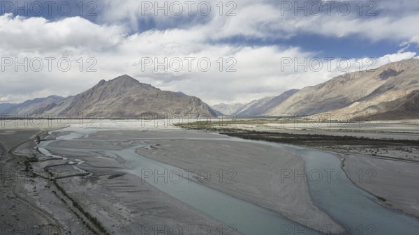 Extensive river landscape on the Indus with mountains in the background under a cloud cover, trekking in Ladakh, Himalayas, India