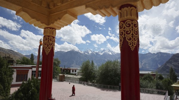 View across the courtyard of a Buddhist monastery to mountains surrounded by colorful, decorated pillars, trekking in Ladakh, Himalayas, India