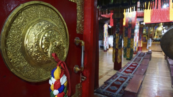 View through the imposing door, magnificent interior of a Buddhist temple with red carpets and golden ornaments, trekking in Ladakh, Himalayas, India