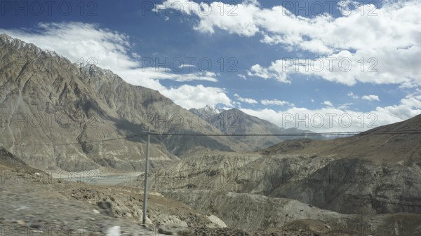 Wide mountain landscape with river valley and power lines under partly cloudy sky, trekking in Ladakh, Himalayas, India