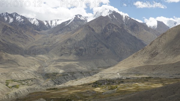 Secluded village at the foot of snow-capped mountains under a cloudy sky, trekking in Ladakh, Himalayas, India