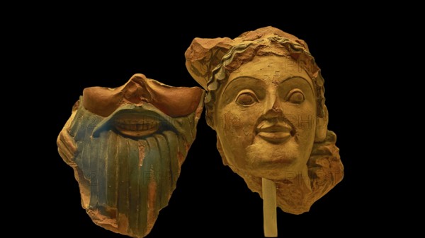 Two ancient clay masks, one with beard and smile, the other with flowing hair, on a dark background, Olympia Archaeological Museum, Ancient Olympia, Peloponnese, Greece