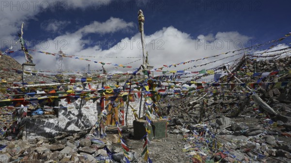 Colourful prayer flags surround a rocky area with statues at Khardug-La Pass and add color to the mountainous landscape, trekking in Ladakh, Himalayas, India