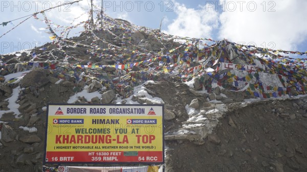 Colourful prayer flags fly next to the Khardung-La Top sign on the summit, trekking in Ladakh, Himalayas, India