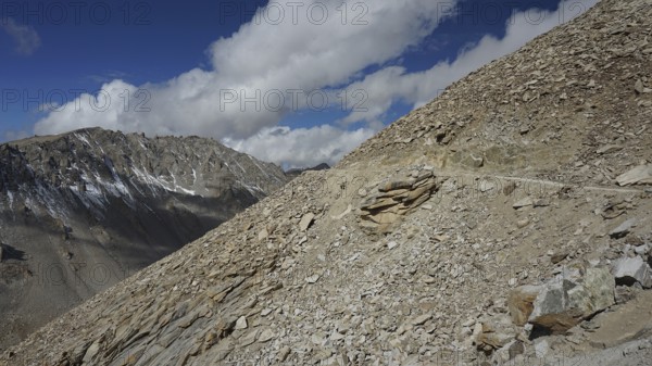 Rocky mountain terrain with road on the mountainside under a sunny sky with scattered clouds, trekking in Ladakh, Himalayas, India