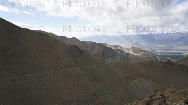 A road along a rocky mountainside that runs through a vast landscape under clear skies, trekking in Ladakh, Himalayas, India