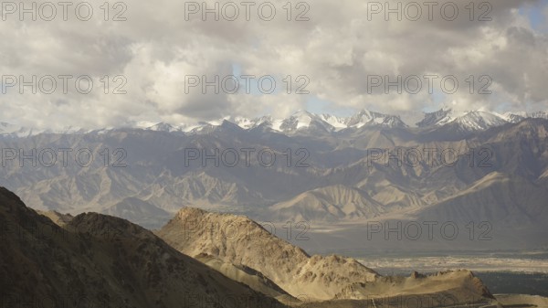 Wide panorama with mountains and snowy peaks under cloudy sky, trekking in Ladakh, Himalayas, India
