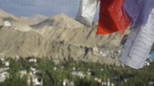 Close-up of prayer flags in foreground with mountain landscape in background under cloudy sky, trekking in Ladakh, Himalayas, India