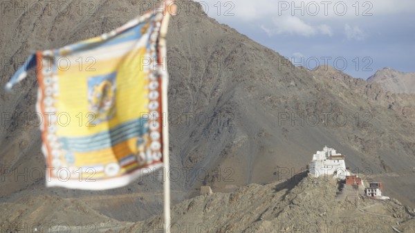 Tibetan Buddhist prayer flag with Namgyal Tsemo Buddhist monastery surrounded by mountains and sky, Leh, trekking in Ladakh, Himalayas, India